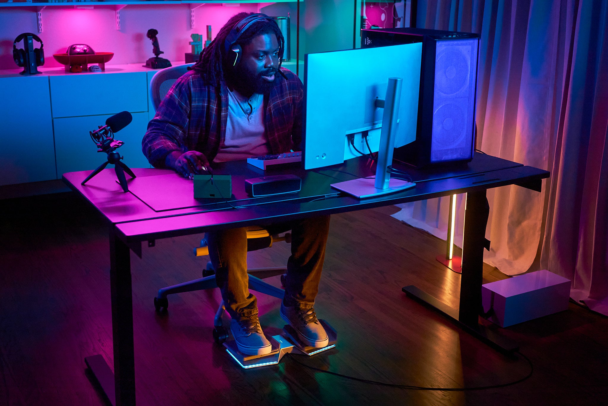 Person sitting at a desk with a computer setup in a room with colorful lighting with his sneakers placed flat on each of the two pedals of the Glydr foot controller.